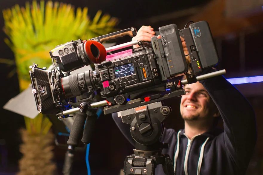 Behind-the-scenes colour photograph of a cinema camera being adjusted on a tripod