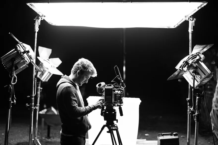 Wide black-and-white photograph of a camera setup surrounded by studio lighting