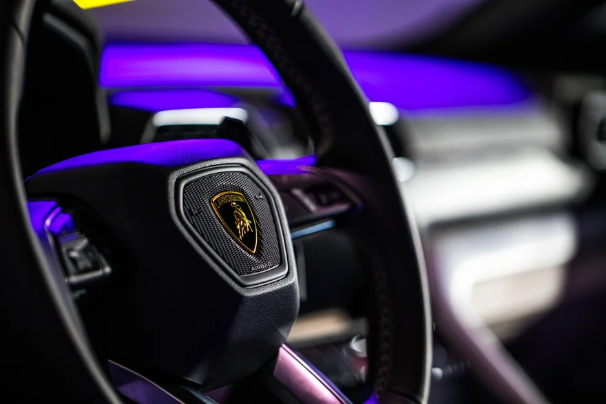 Steering wheel detail with purple light across a dark car interior
