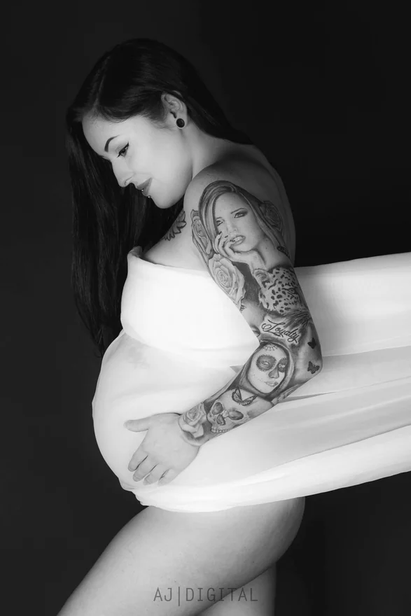 Black-and-white studio portrait with white fabric and a tattooed arm against a dark background
