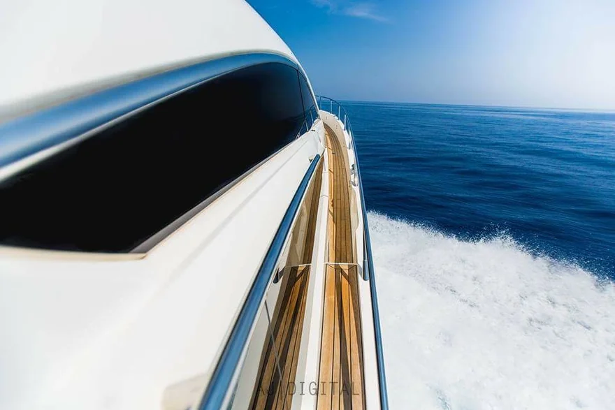 View along the side deck of a yacht moving across blue water